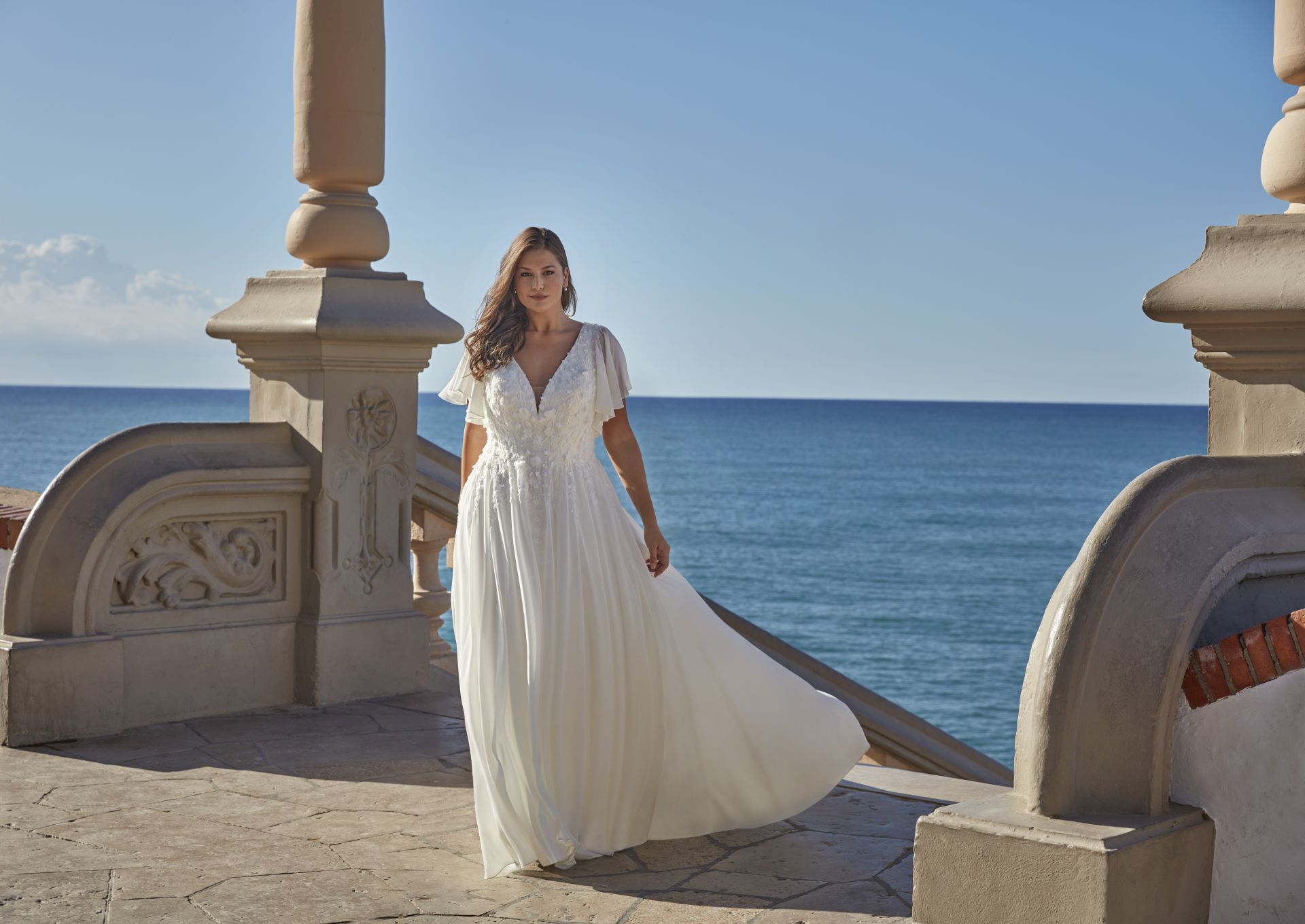 Eine Frau in einem weißen Kleid steht auf einem Balkon mit Blick auf den Ozean.