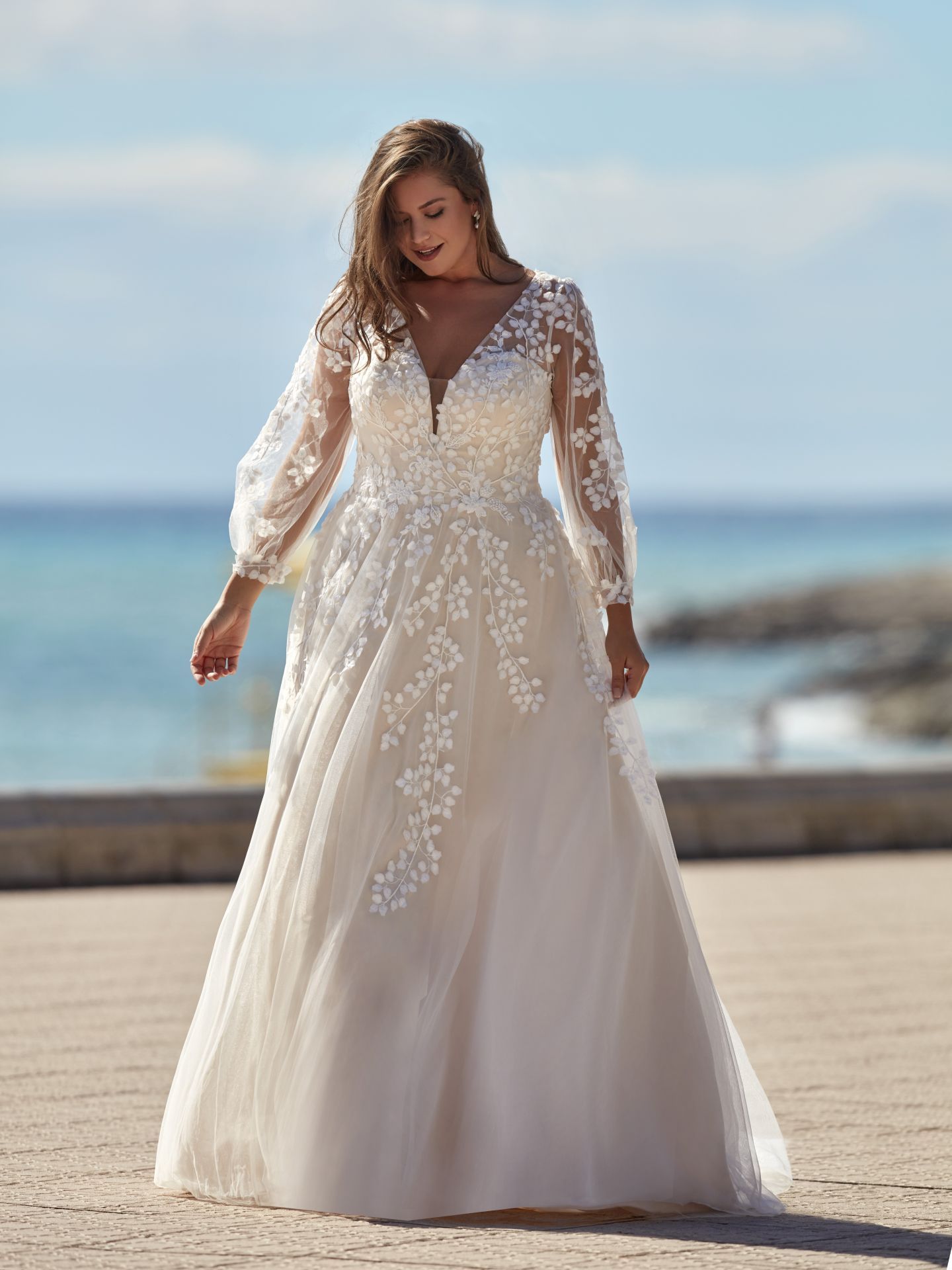 Eine Frau mit Übergröße trägt ein weißes Brautkleid mit langen Ärmeln.