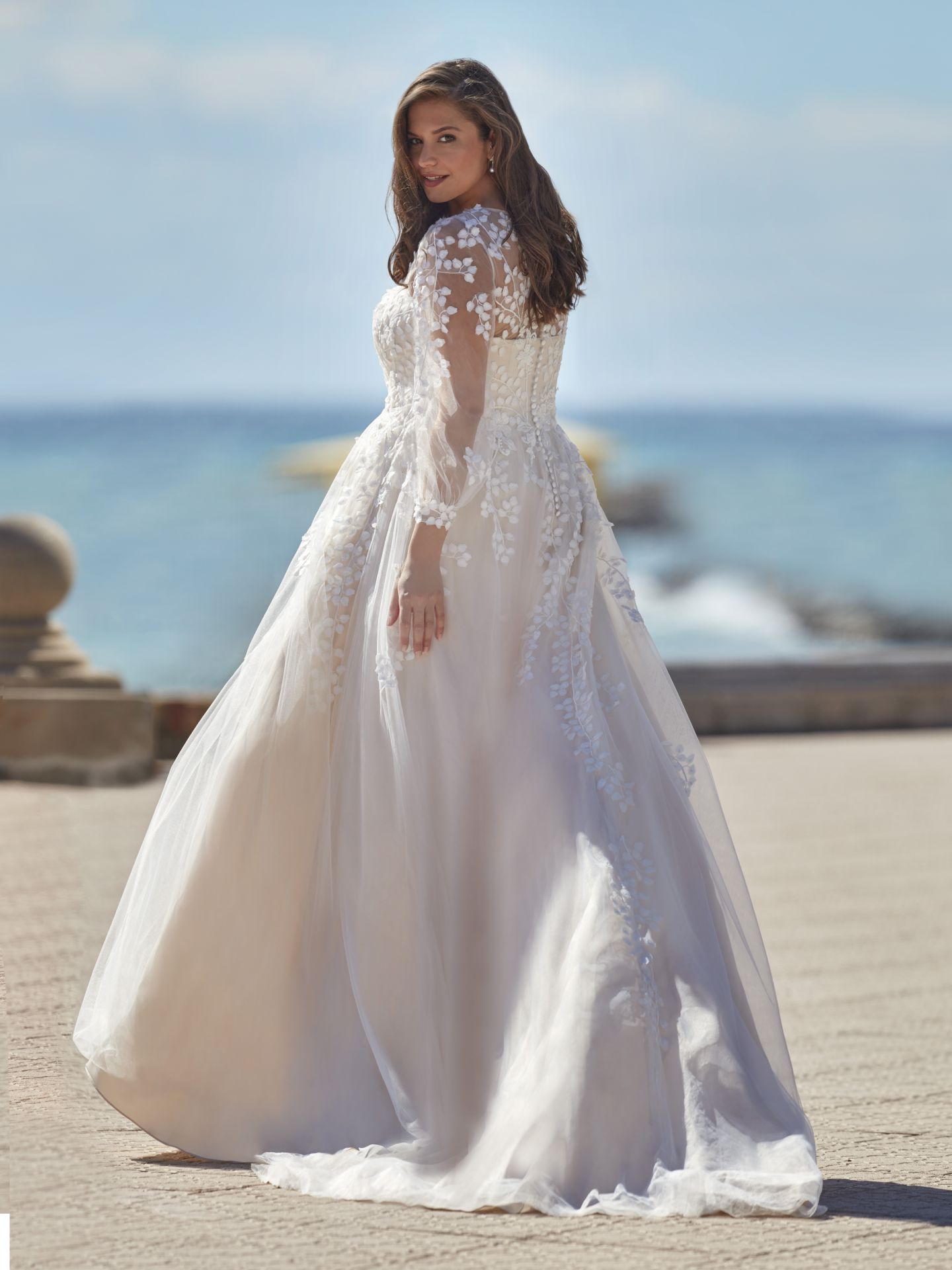 Eine Frau in einem weißen Brautkleid steht an einem Strand.