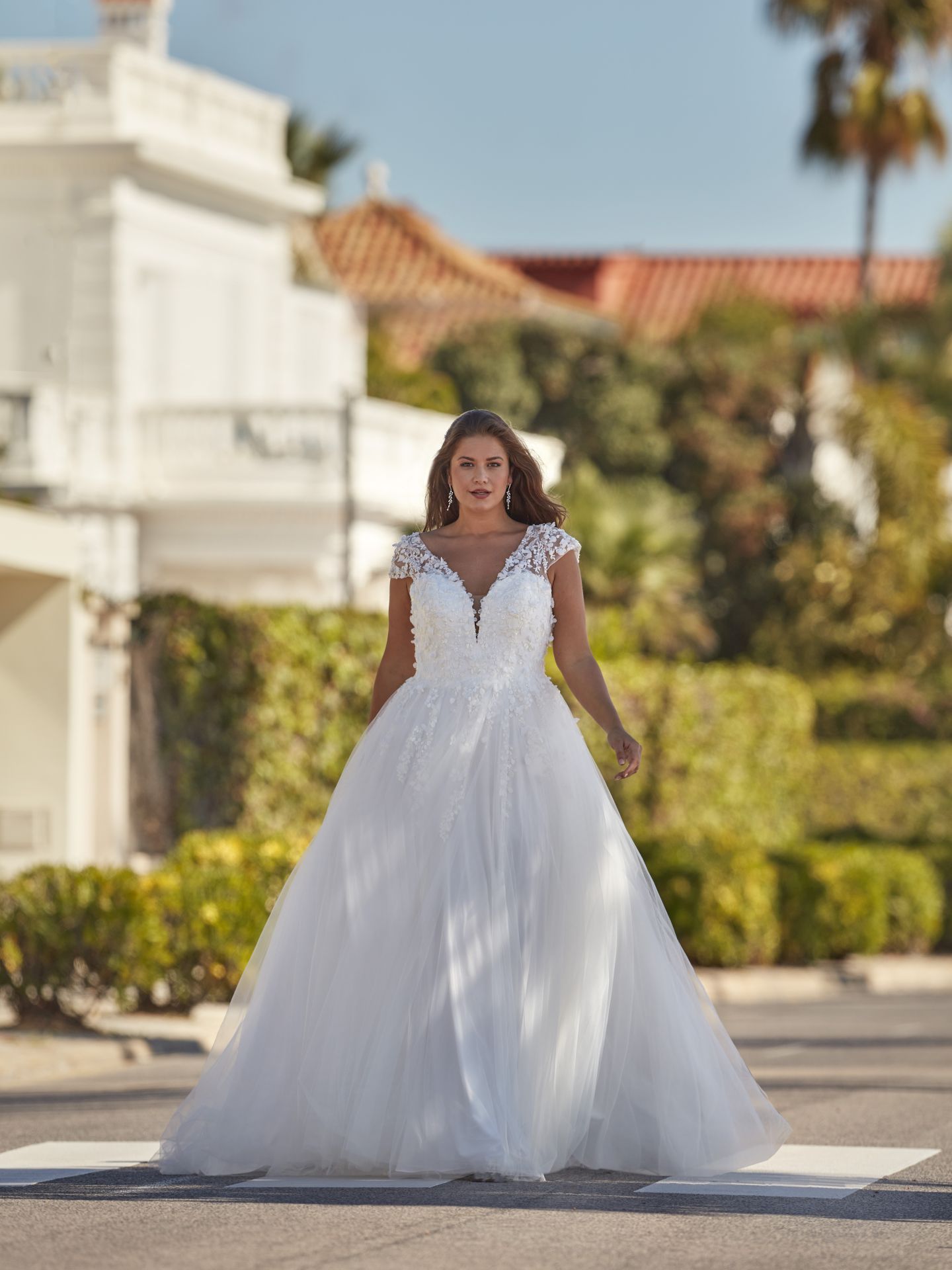 Eine Frau in einem weißen Brautkleid steht auf einem Bürgersteig vor einem Gebäude.