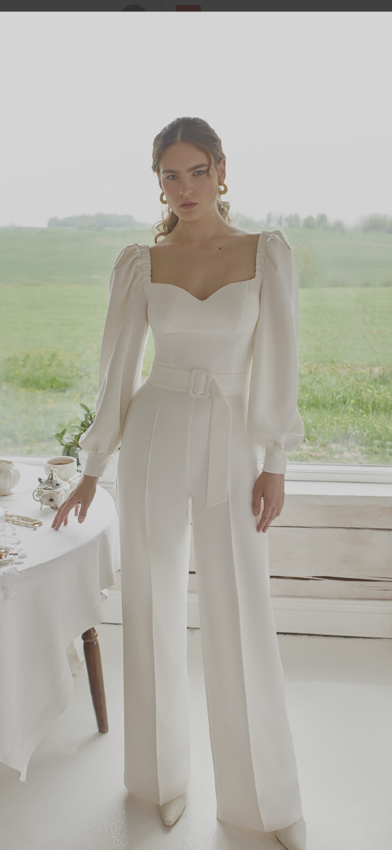 Eine Frau in einem weißen Overall steht vor einem Fenster.