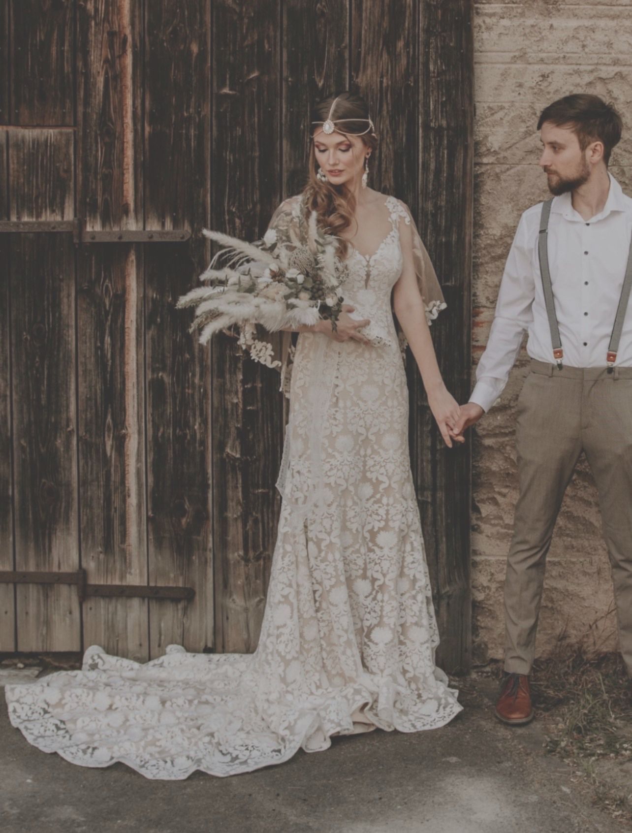 Eine Braut und ein Bräutigam halten vor einem Holzgebäude Händchen.