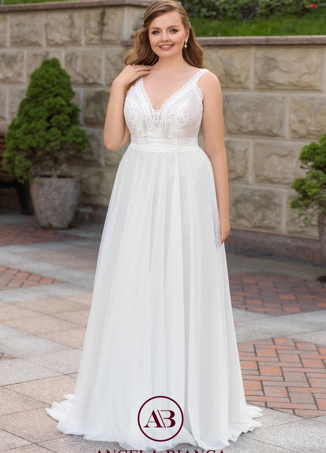 Eine Frau in einem weißen Brautkleid steht vor einer Backsteinmauer.