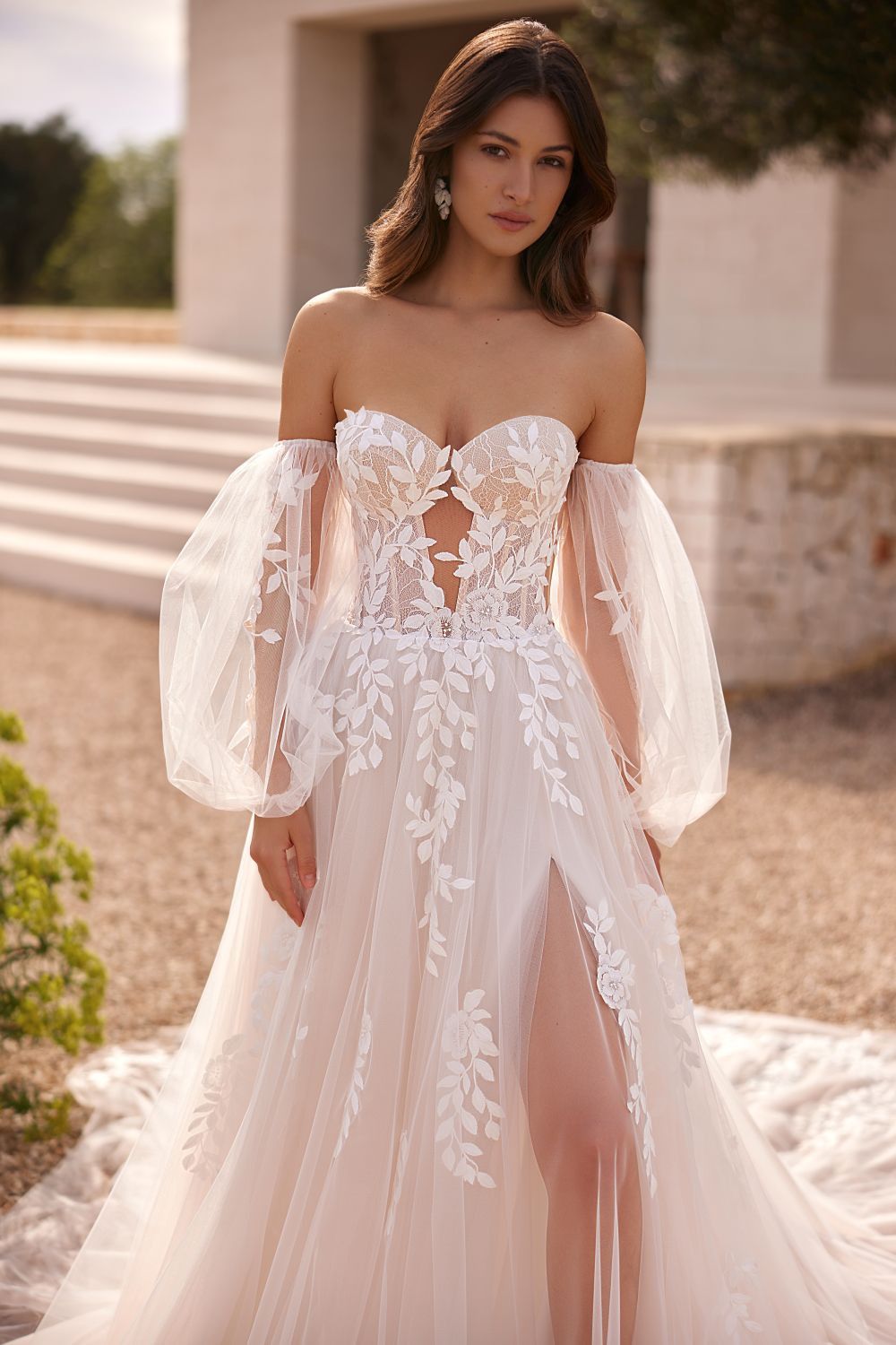 Eine Frau trägt ein Brautkleid mit langen Ärmeln und einem hohen Schlitz.