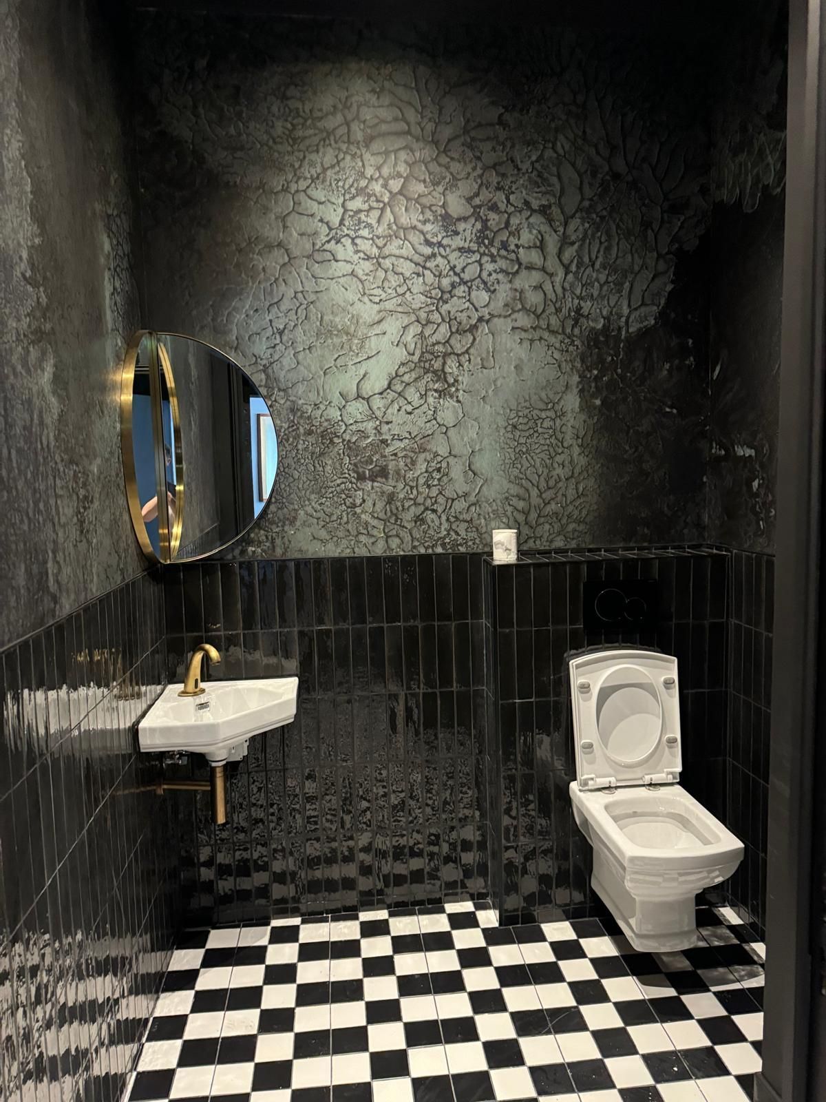 A bathroom with a toilet , sink , mirror and checkered floor.