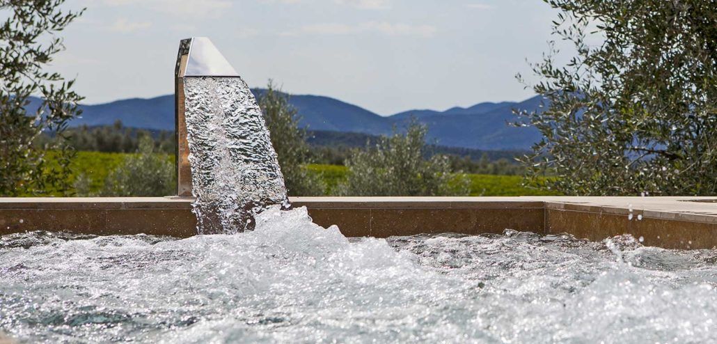 Una fontana spruzza acqua in una piscina con le montagne sullo sfondo.
