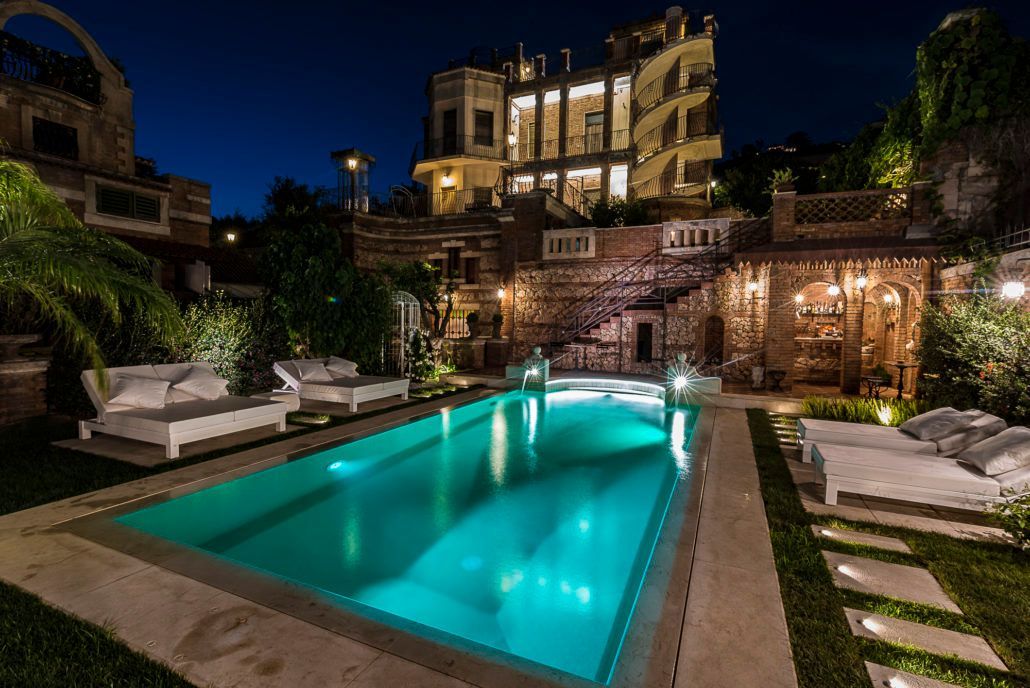 Una grande piscina è illuminata di notte di fronte a un grande edificio.