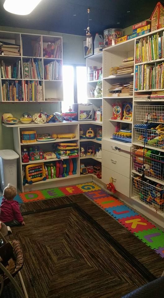 Child's playroom with shelves filled with books and toys. A child is seated on the floor with a colorful alphabet mat.
