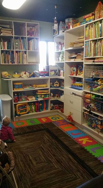 Child's playroom with shelves full of toys and books. A child sits on the floor near colorful alphabet puzzle mats.