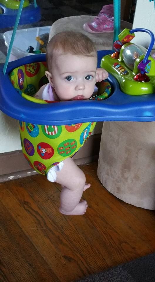 Baby in a colorful jumper, looking at the camera, wooden floor in the background.