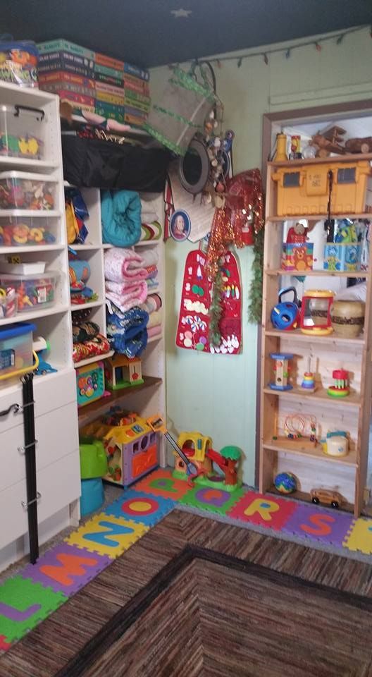 Playroom filled with toys on shelves and the floor, with colorful floor mats.