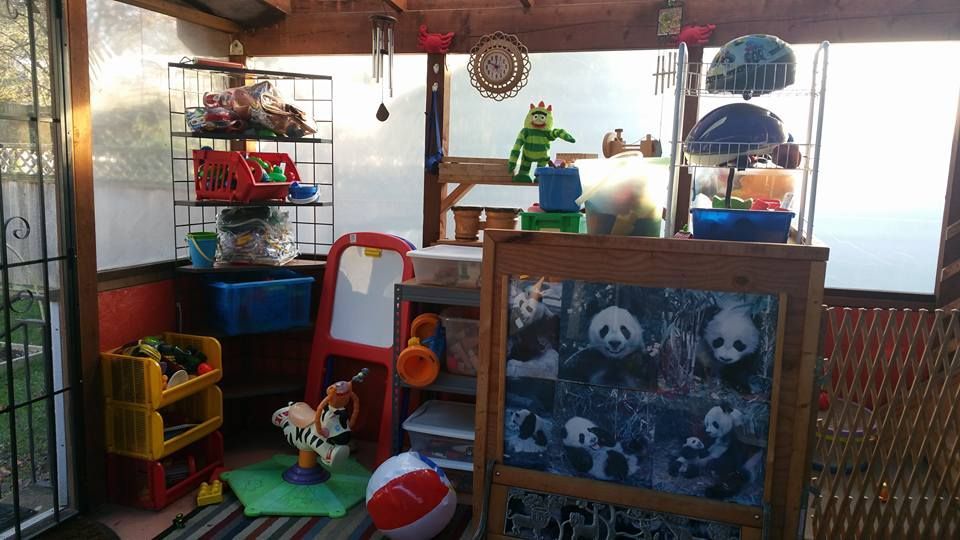 Playroom with toys, chalkboard, shelves, and seating inside a sunroom.