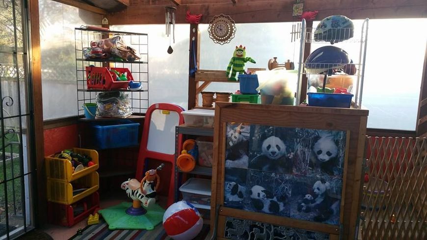 Playroom filled with toys; shelving units, a chalkboard, and a light-filled setting.