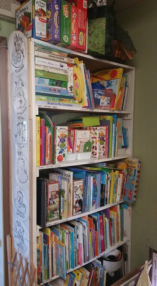 White bookshelf filled with children's books, set against a green wall. Includes various colors and book sizes.