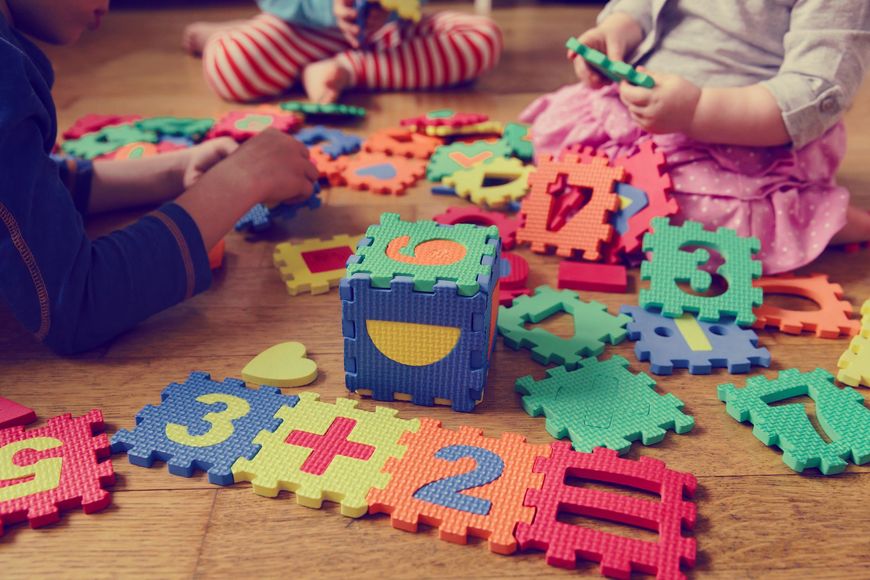 Children playing with colorful number puzzles on a wooden floor.