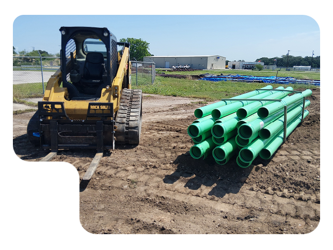 Yellow excavator beside stacked green pipes at a construction site under clear skies
