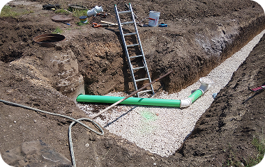 Trench with gravel base, green pipe, and ladder in an excavated construction site.
