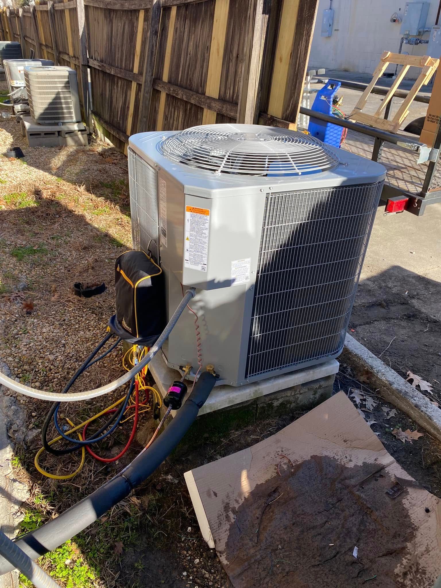 A large air conditioner is sitting on the ground next to a fence.