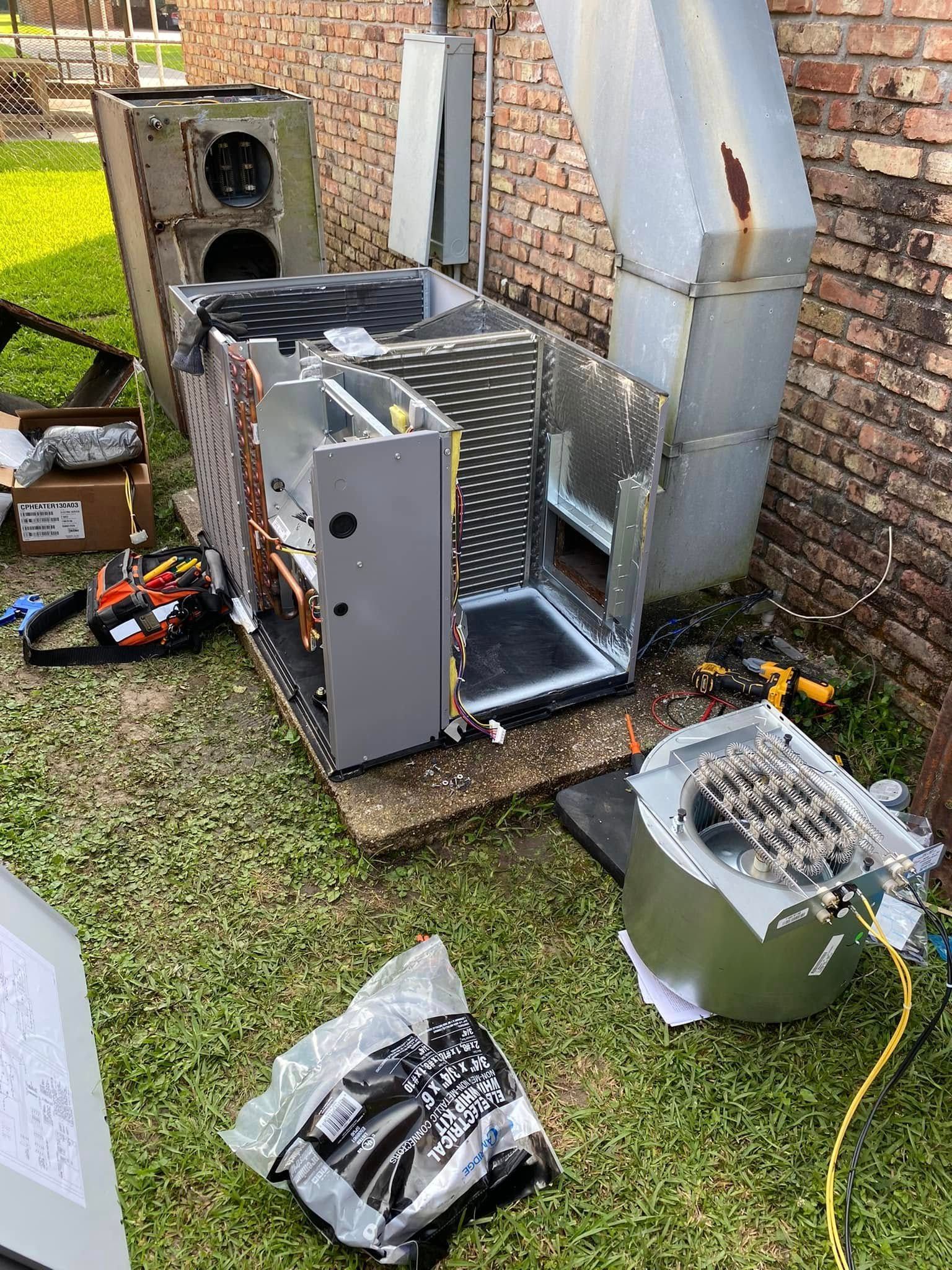 A broken air conditioner is sitting on the grass next to a brick wall.