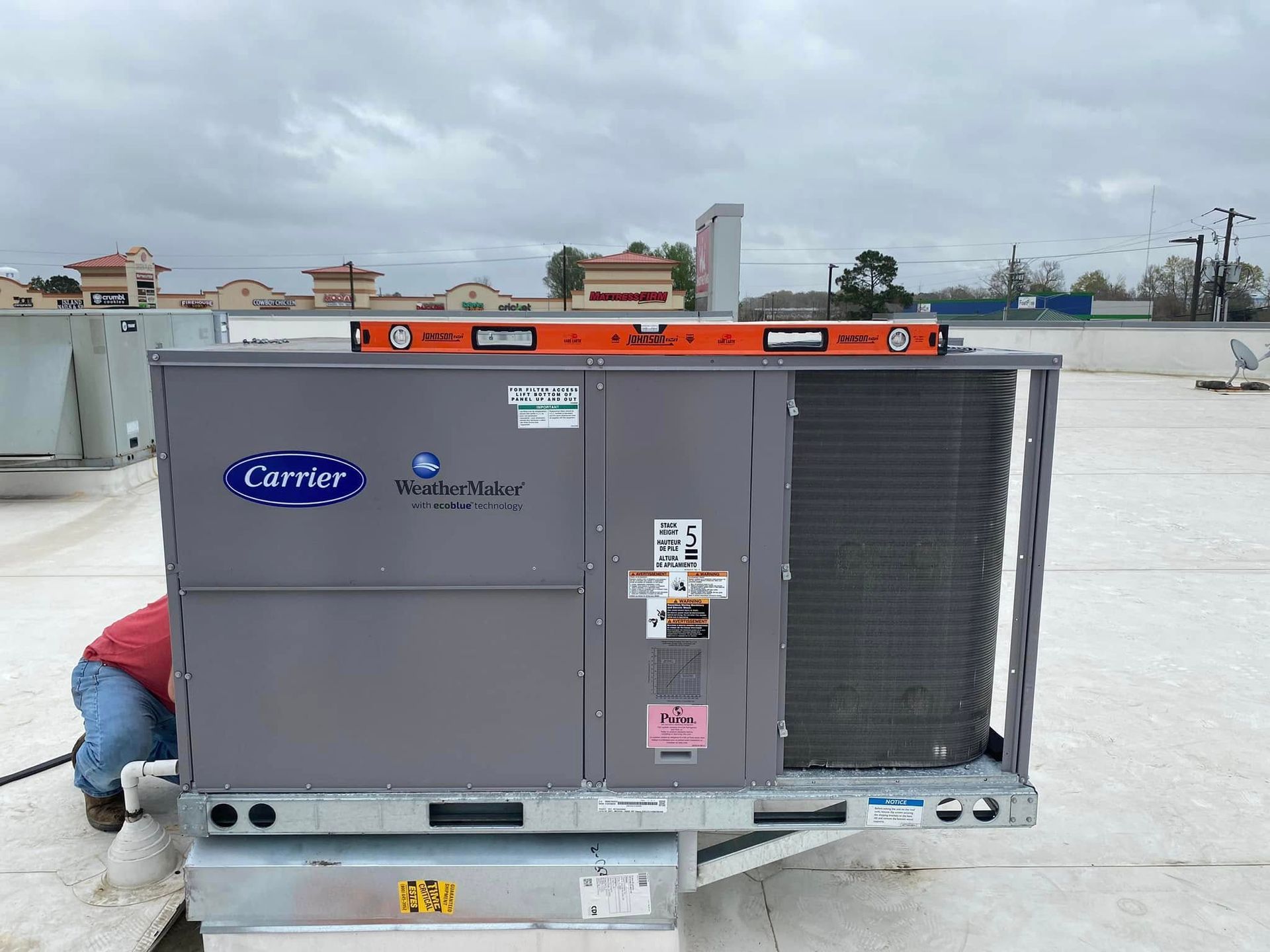 A man is working on a carrier air conditioner on a roof.