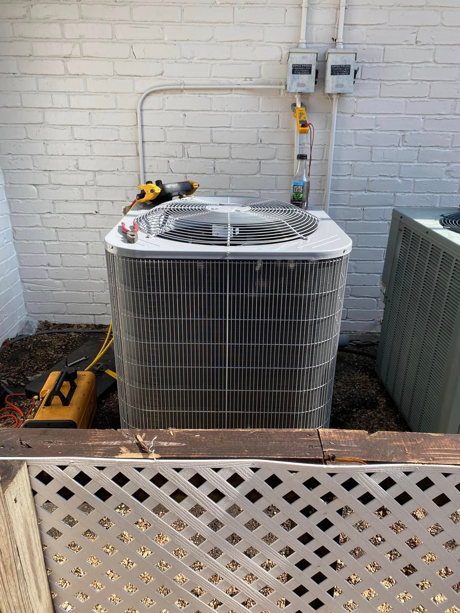 A large air conditioner is sitting in front of a white brick wall.
