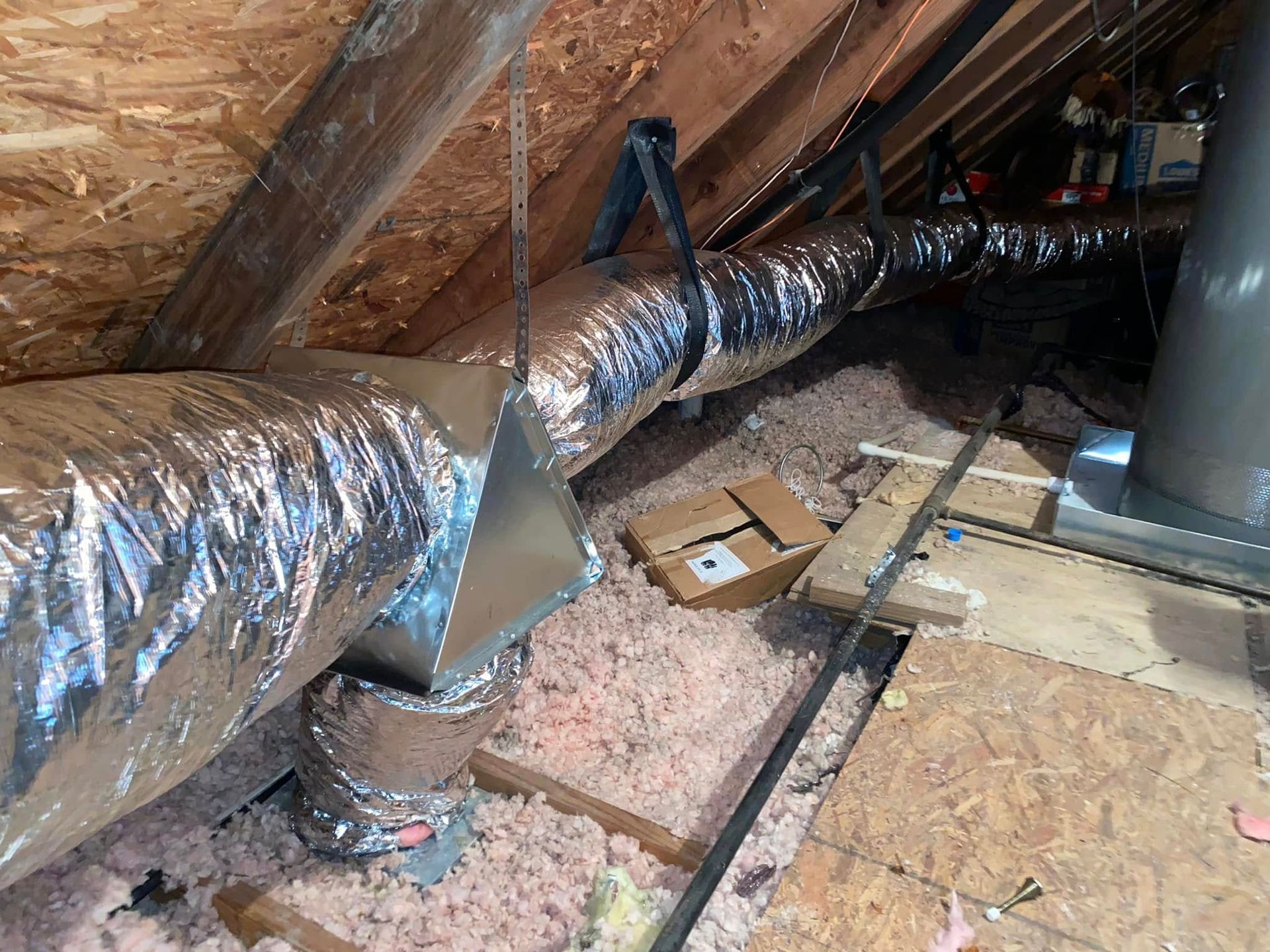 A duct is hanging from the ceiling of an attic.
