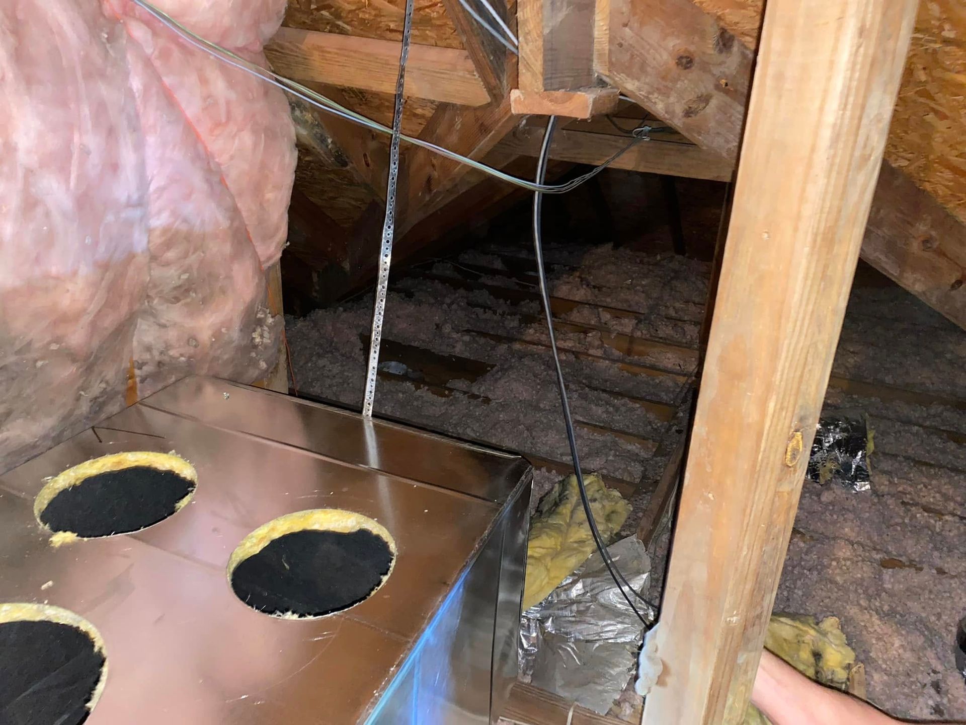 A person is holding a metal box in an attic.