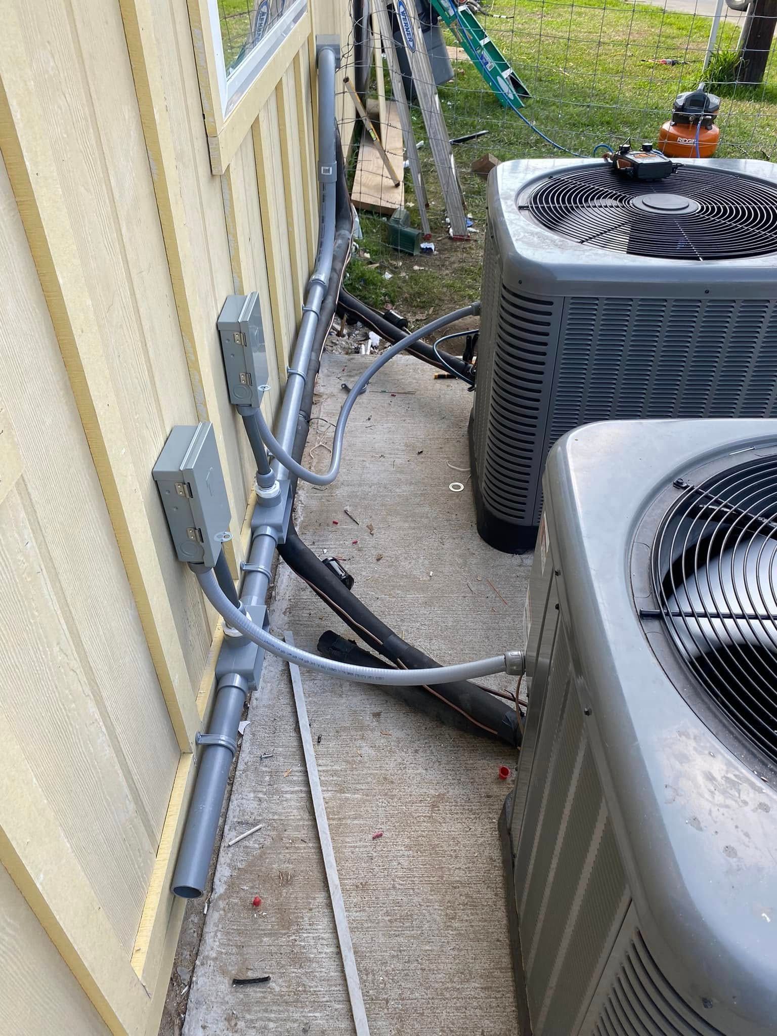 Two air conditioners are sitting next to each other on the side of a house.