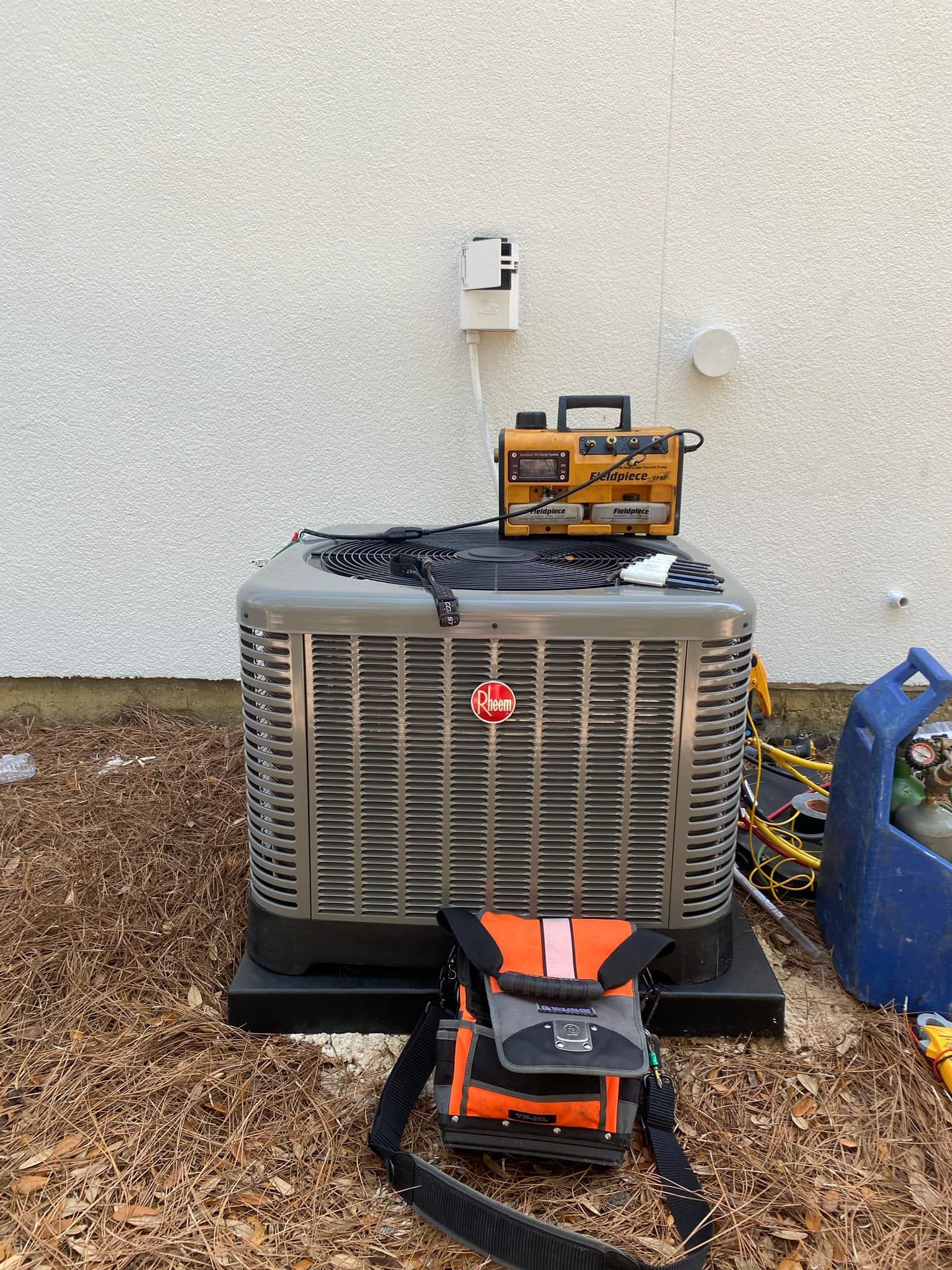 An air conditioner is sitting on the ground next to a toolbox.