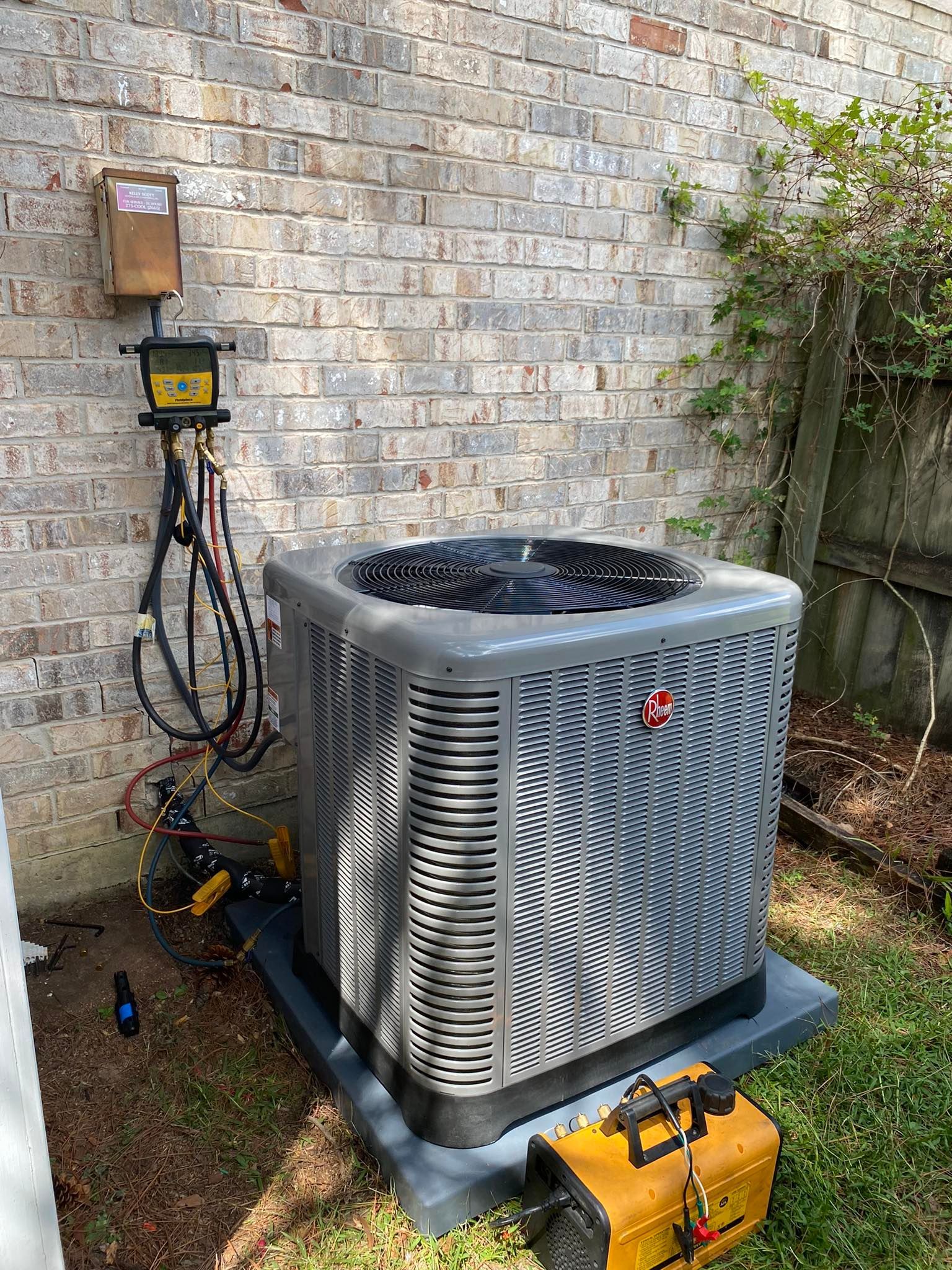 An air conditioner is sitting on top of a concrete platform in front of a brick wall.