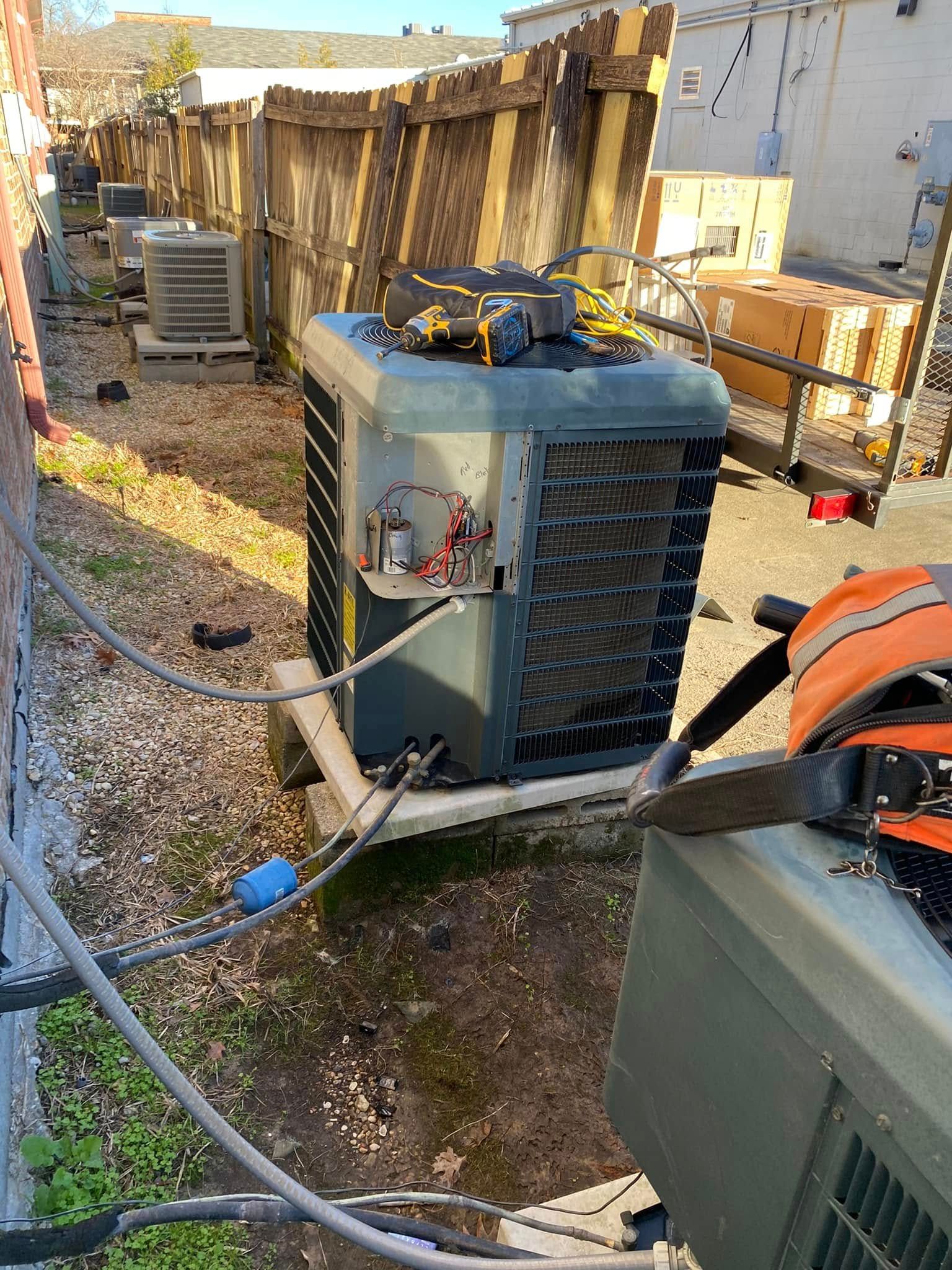 A broken air conditioner is sitting in the dirt next to a fence.