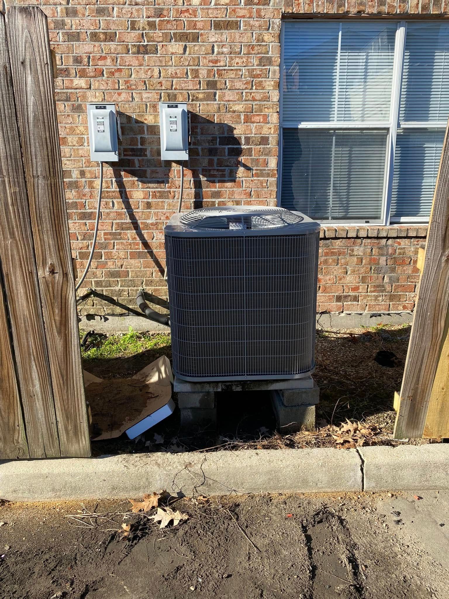 A black air conditioner is sitting in front of a brick building.