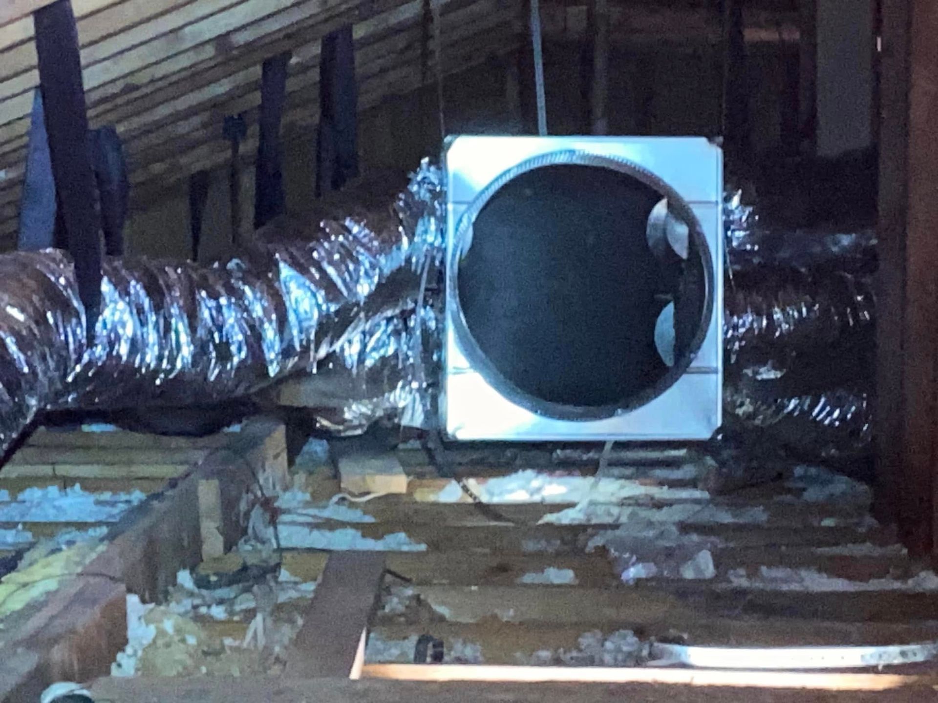 A fan is hanging from the ceiling of an attic.