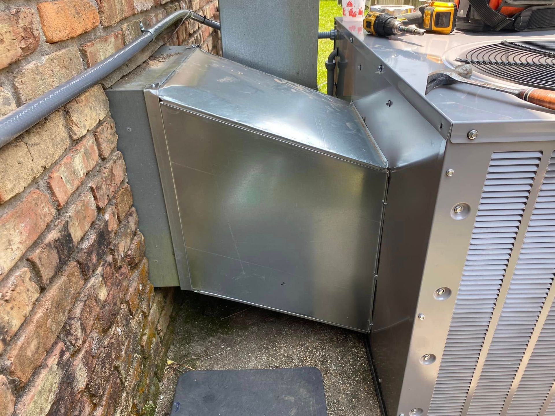 A metal box is sitting next to a brick wall.