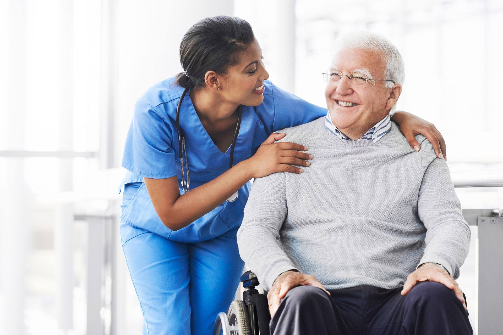 A nurse is putting her arm around an elderly man in a wheelchair.