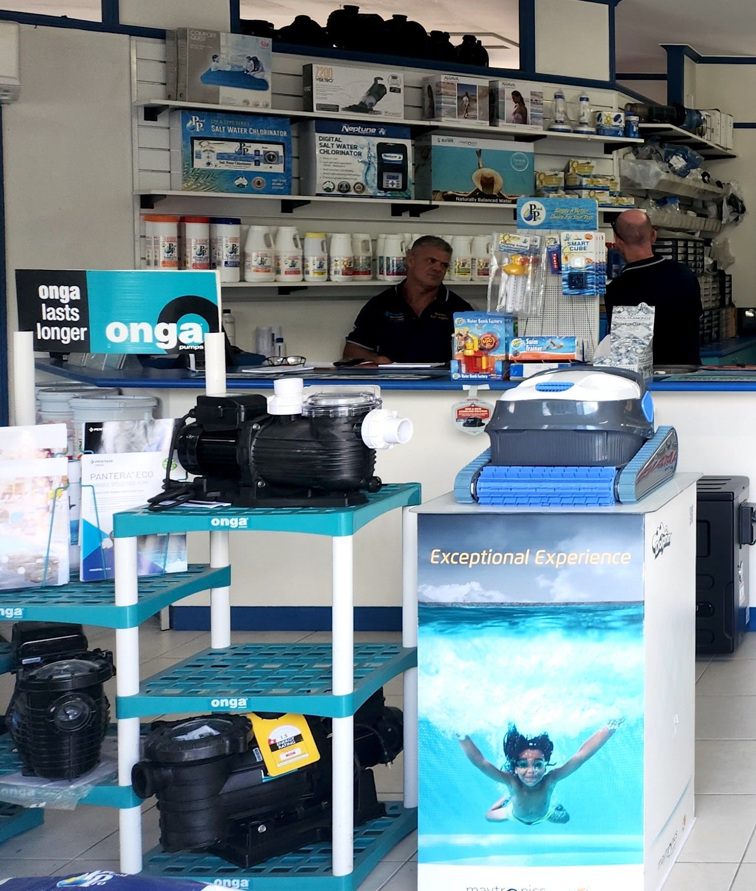 A man is sitting behind a desk with a display of pool equipment in a store — Pool Equipment Installation in Kewarra Beach QLD