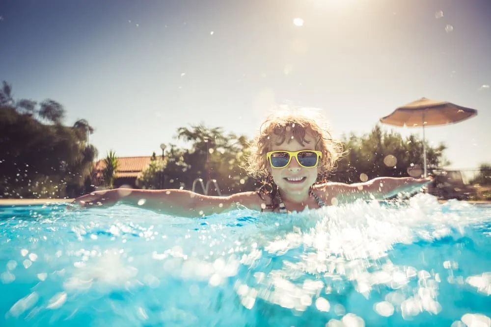 A young girl wearing sunglasses is swimming in a swimming pool — Pool Cleaning in Kewarra Beach QLD