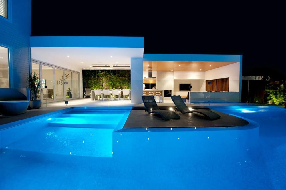 A large swimming pool in front of a house at night — Pool Equipment Installation in Kewarra Beach QLD