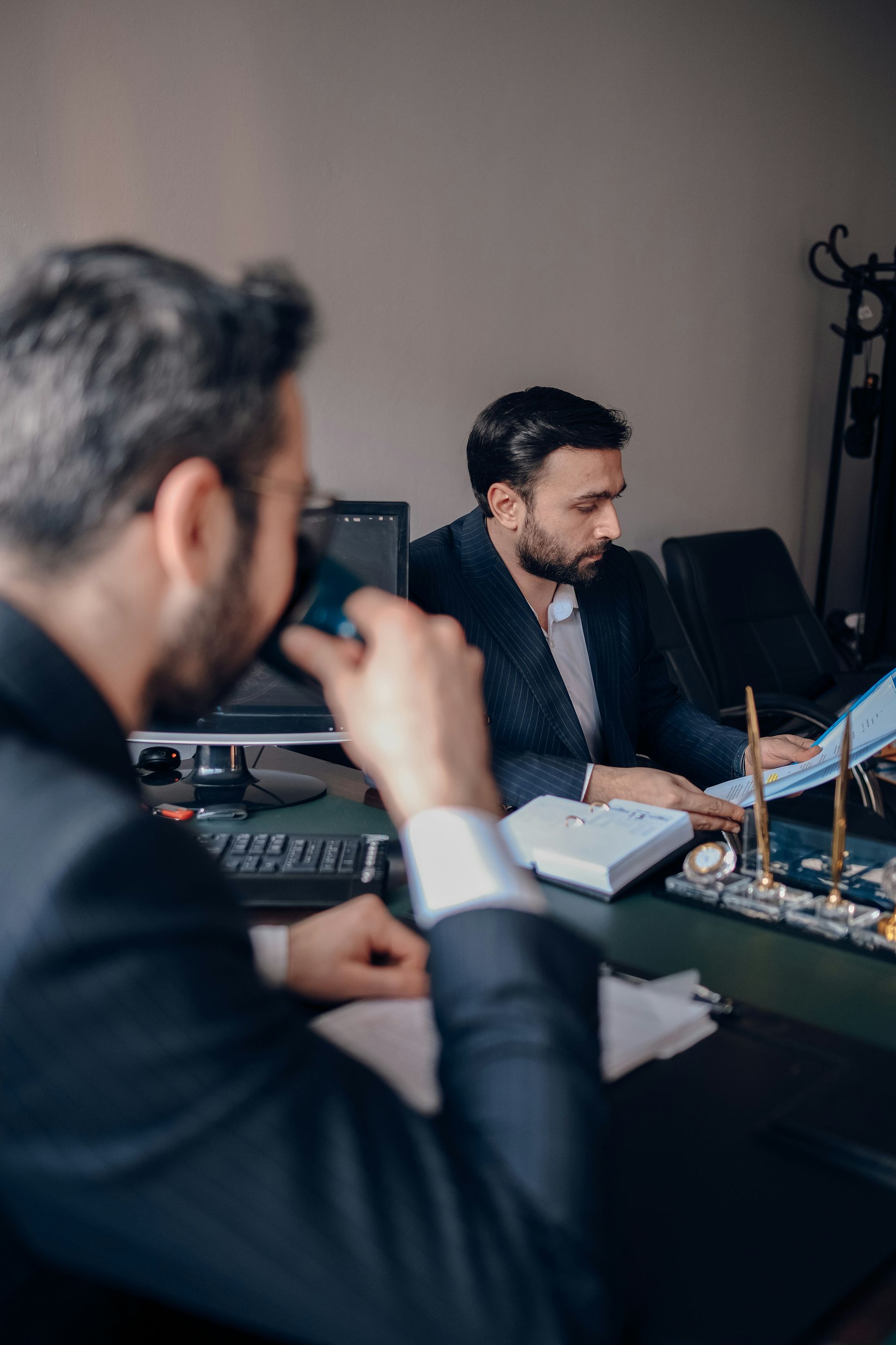 Two men are sitting at a desk in an office looking at papers.