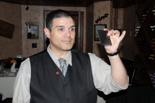 A man in a vest and tie is holding a card in front of a sign that says vino