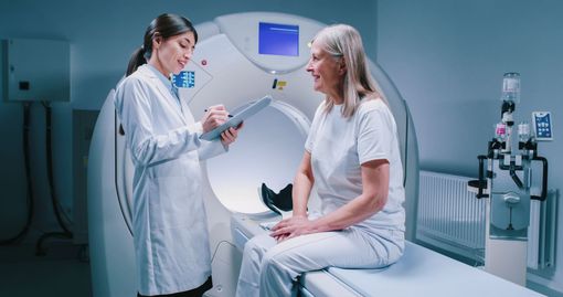 Doctor talking to a patient in a clinic exam room, with an MRI scanner in the background
