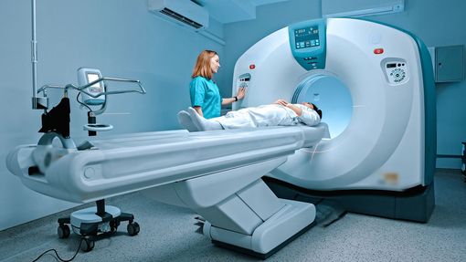 Patient on a CT scanner table while a technician stands beside the white medical imaging machine.