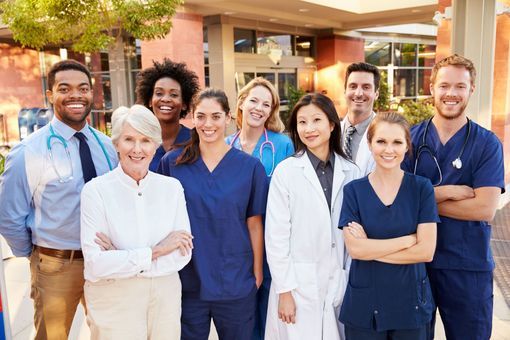 Healthcare staff in scrubs and lab coat smiling outside a clinic entrance