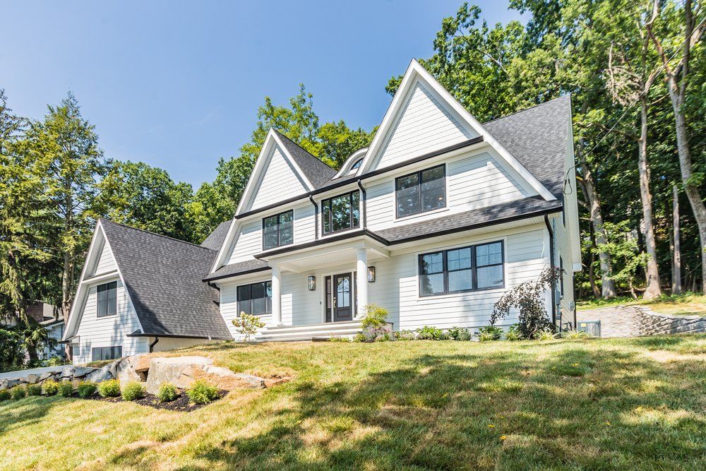 White house with black trim and windows, nestled in a grassy area with trees.