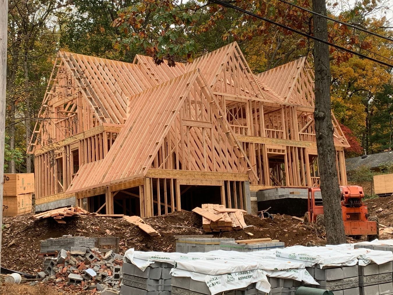 Wooden framework of a house under construction; a partly wooded setting.