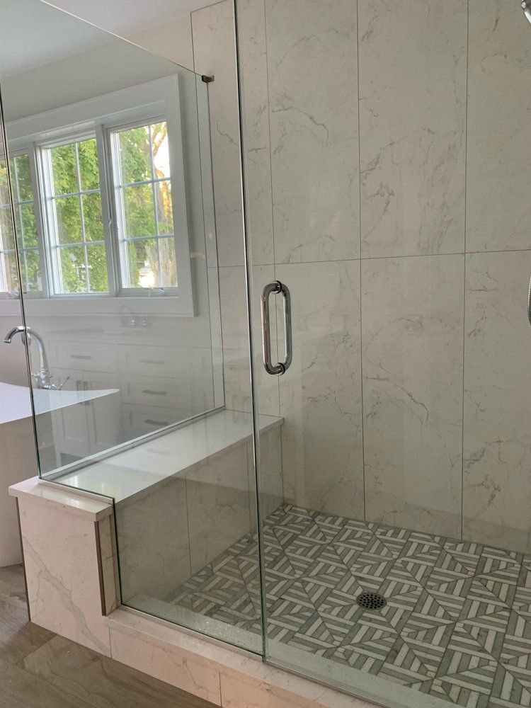 Modern bathroom with glass shower, white marble tile, patterned floor, and window view.