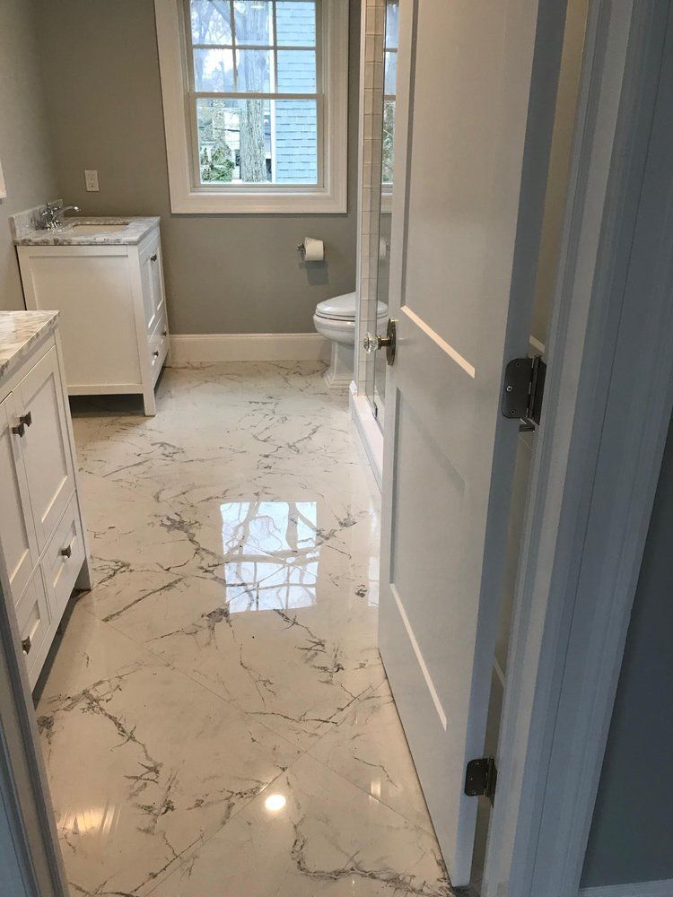 Bathroom with marble floor, white vanity, toilet, and open door. Gray walls, window in the background.