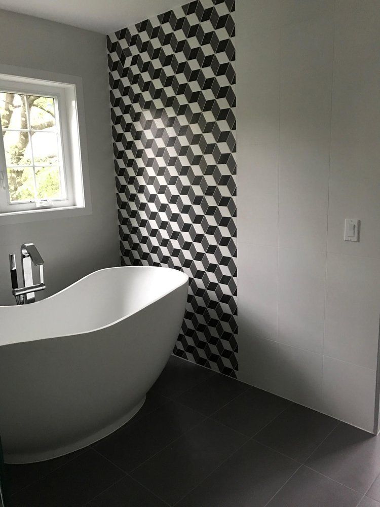 Modern bathroom with white tub, geometric tile accent wall, and dark gray floor.