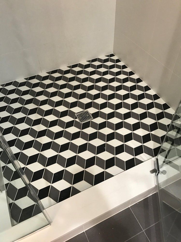 Geometric black, white, and gray tiled shower floor with a drain and glass shower doors.