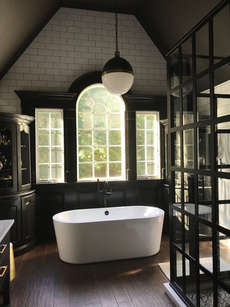 Bathroom with a white tub, arched windows, black trim, and a globe pendant light.